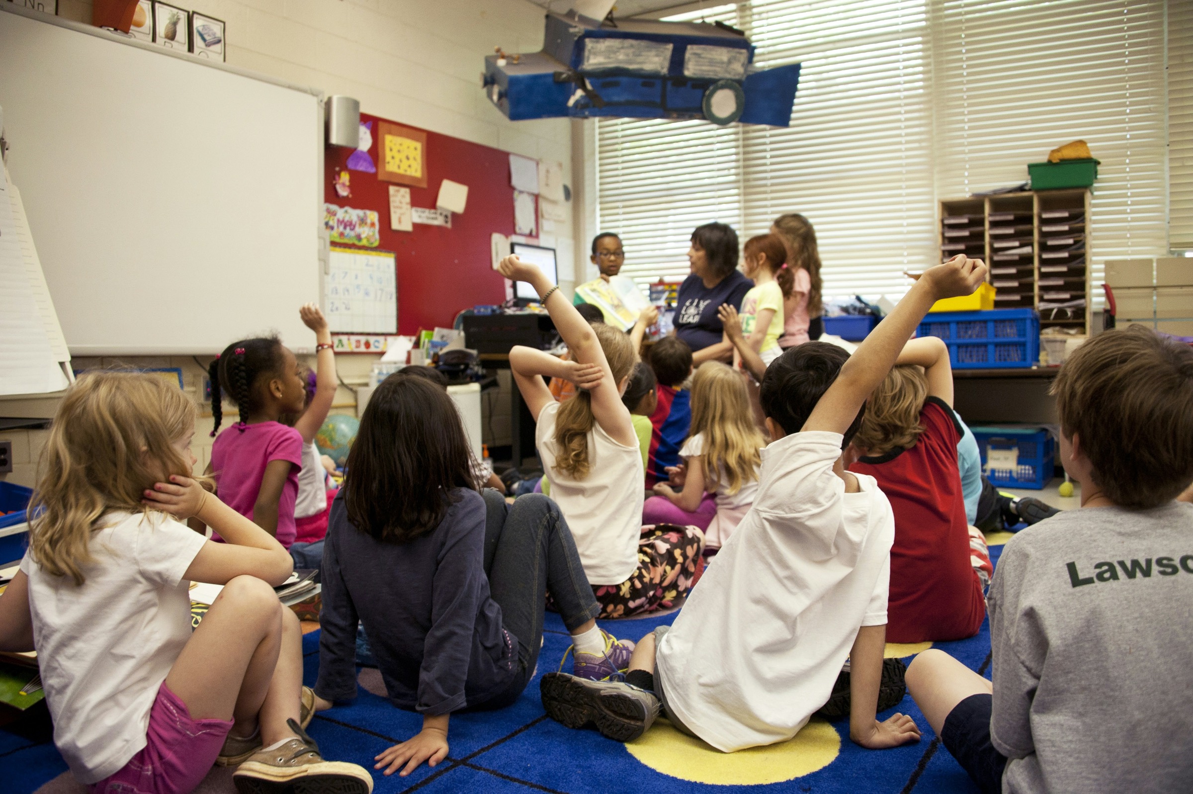 Children sitting on a classroom carpet with hands raised
