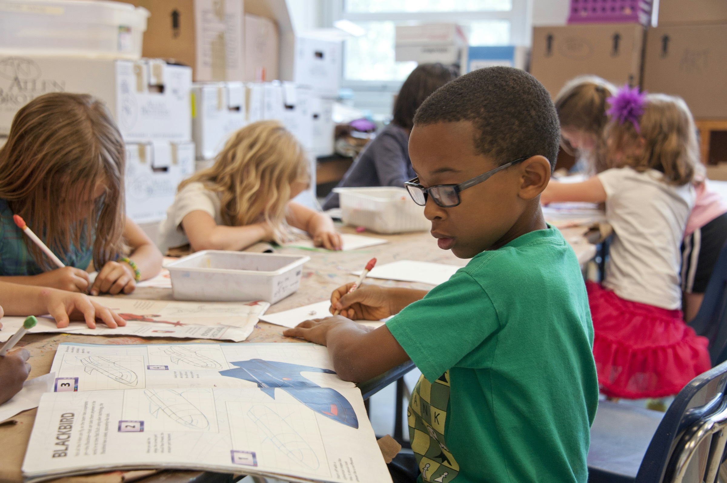 A boy in a green sweater writing at his desk